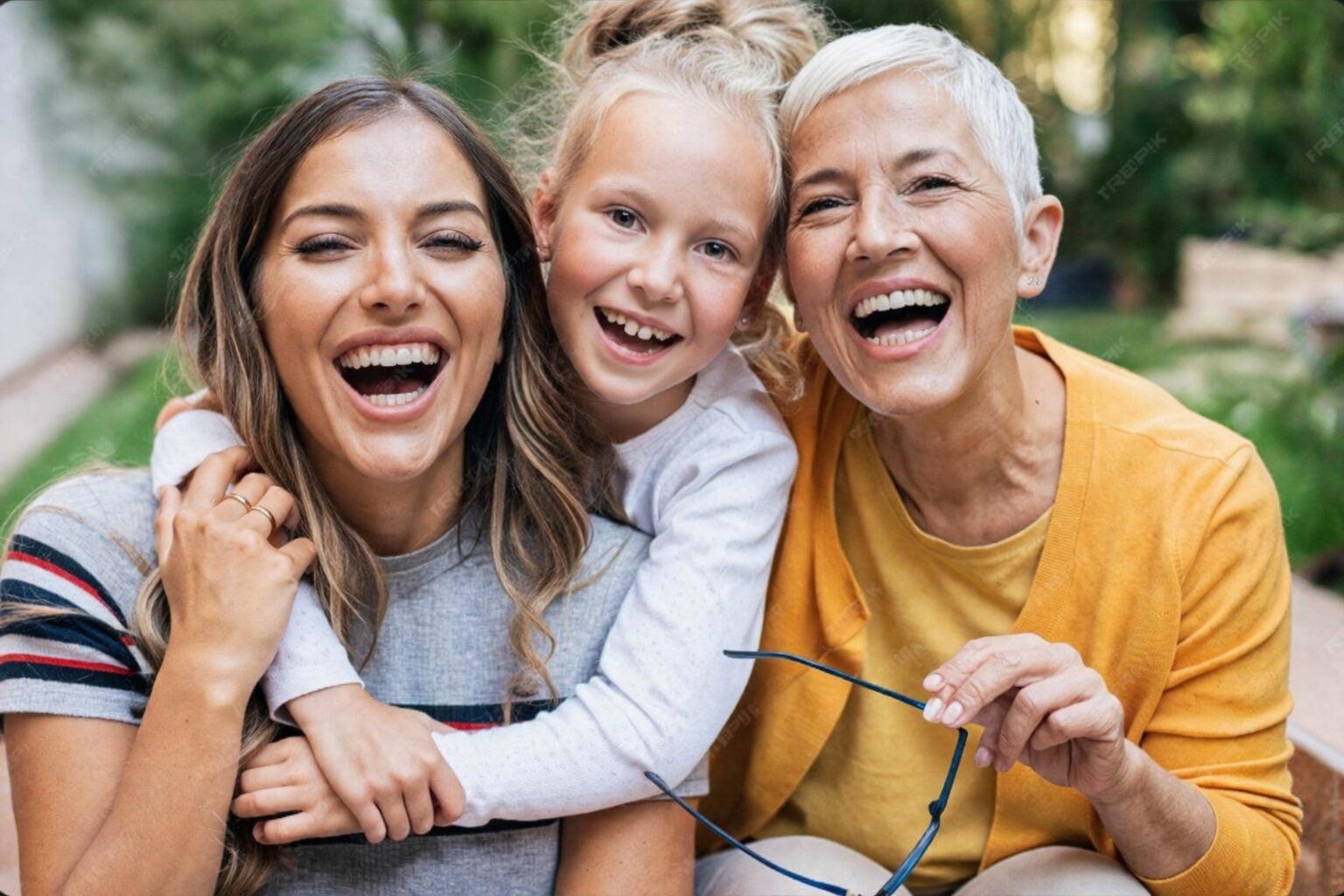 A grandmother, mother and daughter laughing together outdoors
