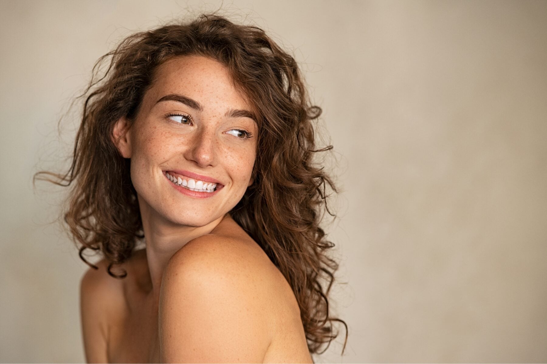 A woman with curly hair smiling over her shoulder